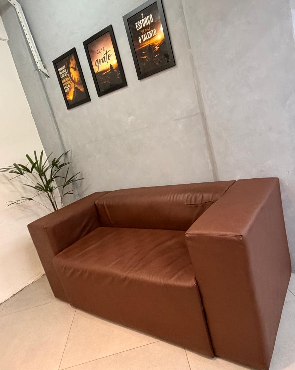 Sofá de couro da espera da Eleve, com os quadros na parede de cimento