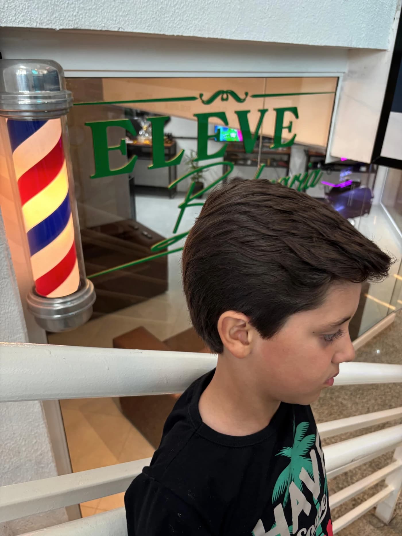 Corte infantil com topete, com a vitrine da Eleve ao fundo